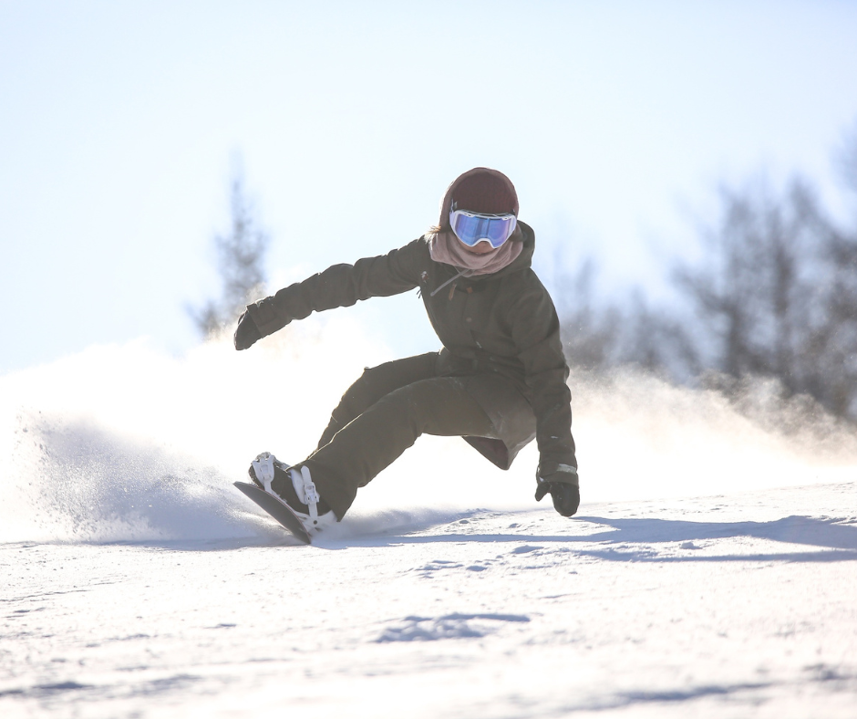 A snowboarder carving through fresh snow on a bright winter day, captured mid-movement against a clear sky.