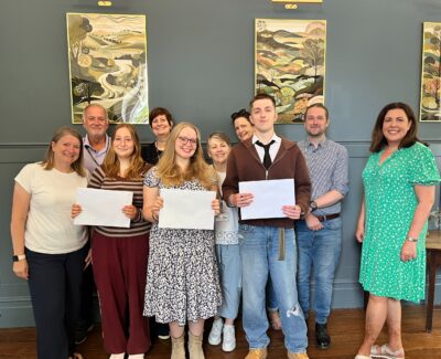 Rookwood School Sixth Form students holding results envelopes and smiling alongside their teachers on A Level results day 2025