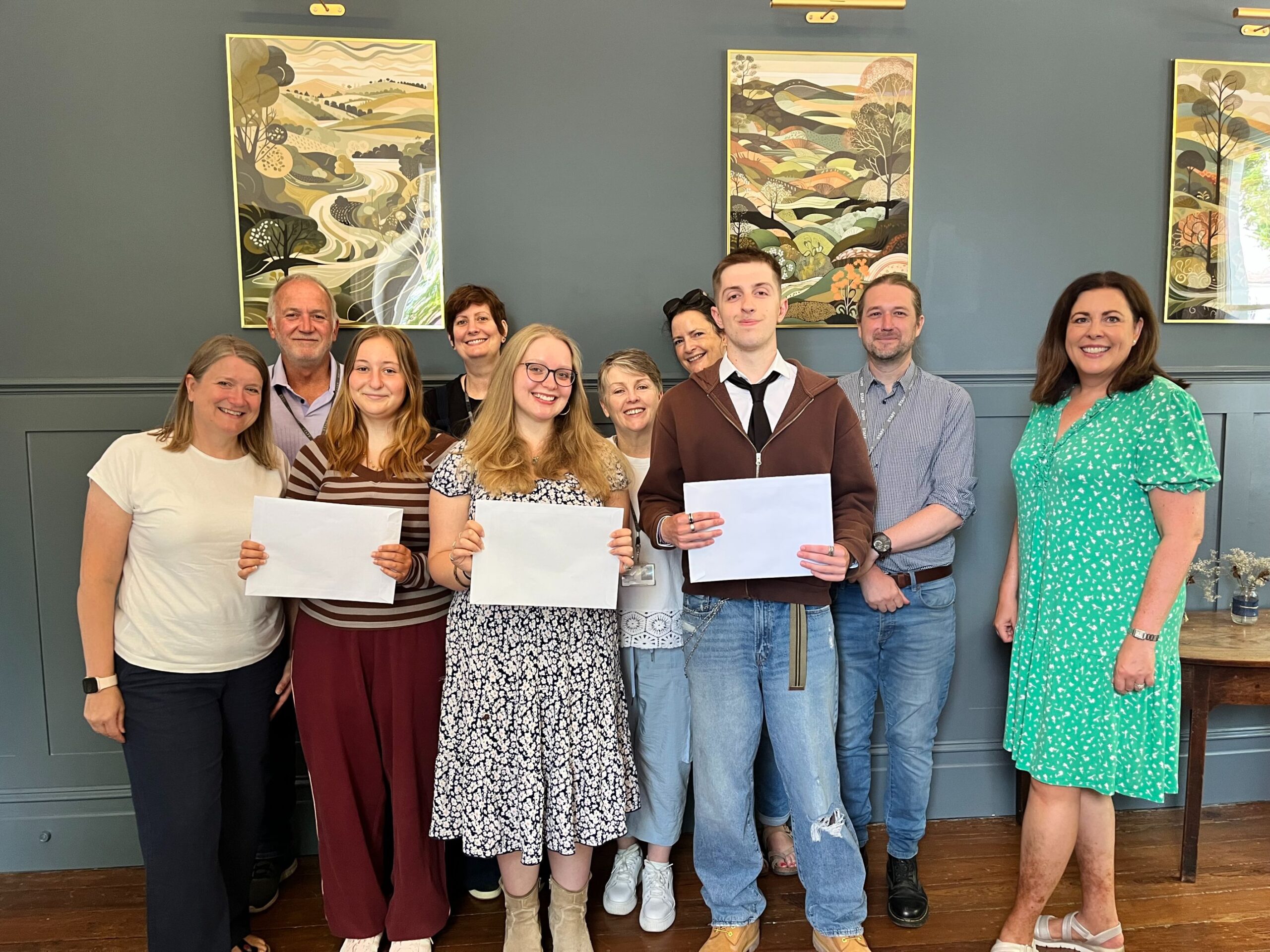 Rookwood School Sixth Form students holding results envelopes and smiling alongside their teachers on A Level results day 2025