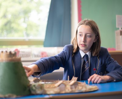 A Rookwood School pupil in a history class pointing at a display of an ancient village.