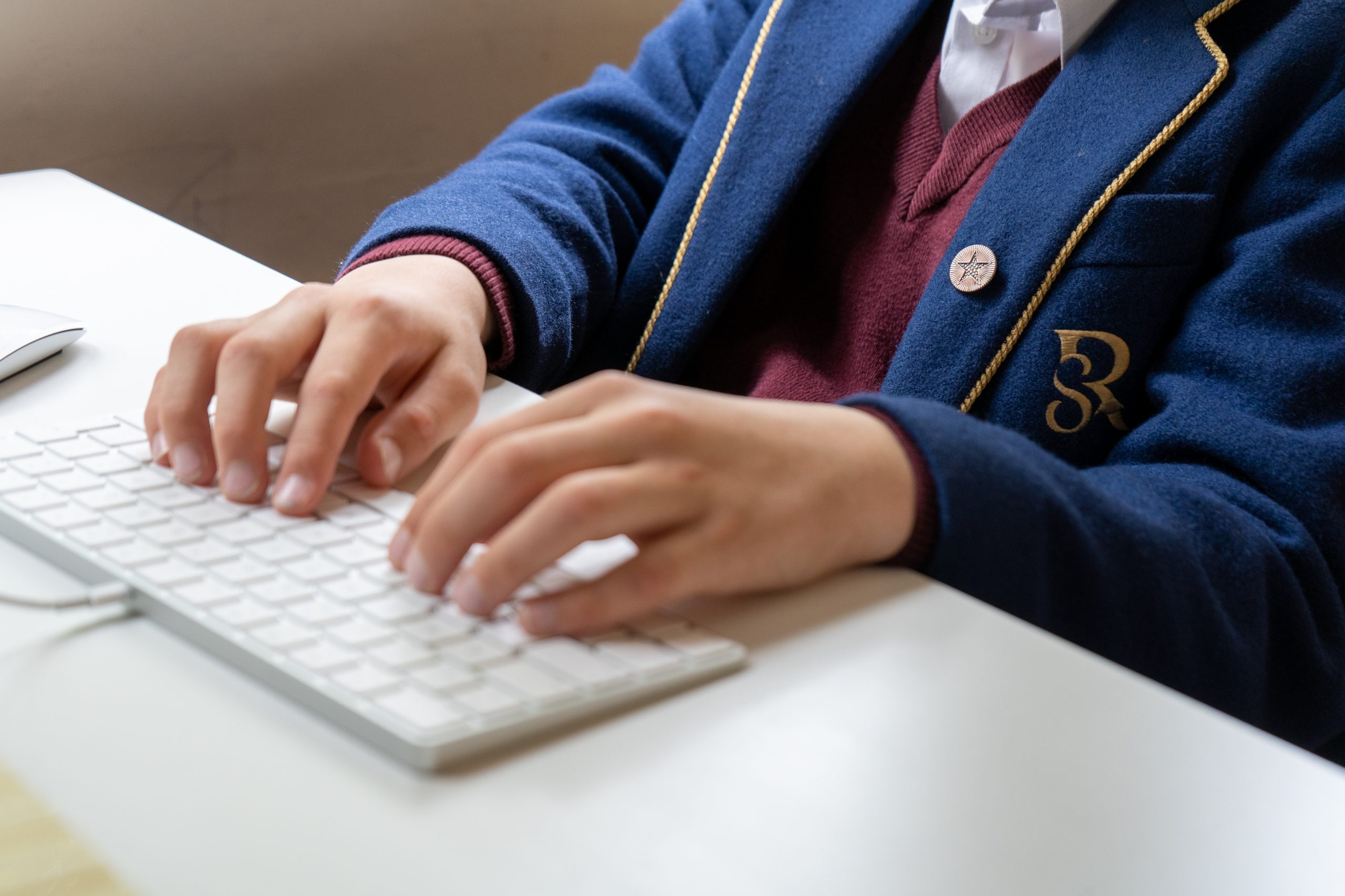 A Rookwood School pupil dressed in uniform typing on a computer keyboard.